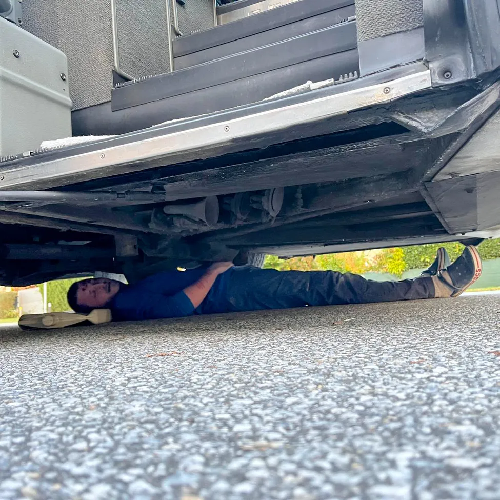 Ein Mann liegt auf dem Boden unter einem Fahrzeug, möglicherweise arbeitet er daran.