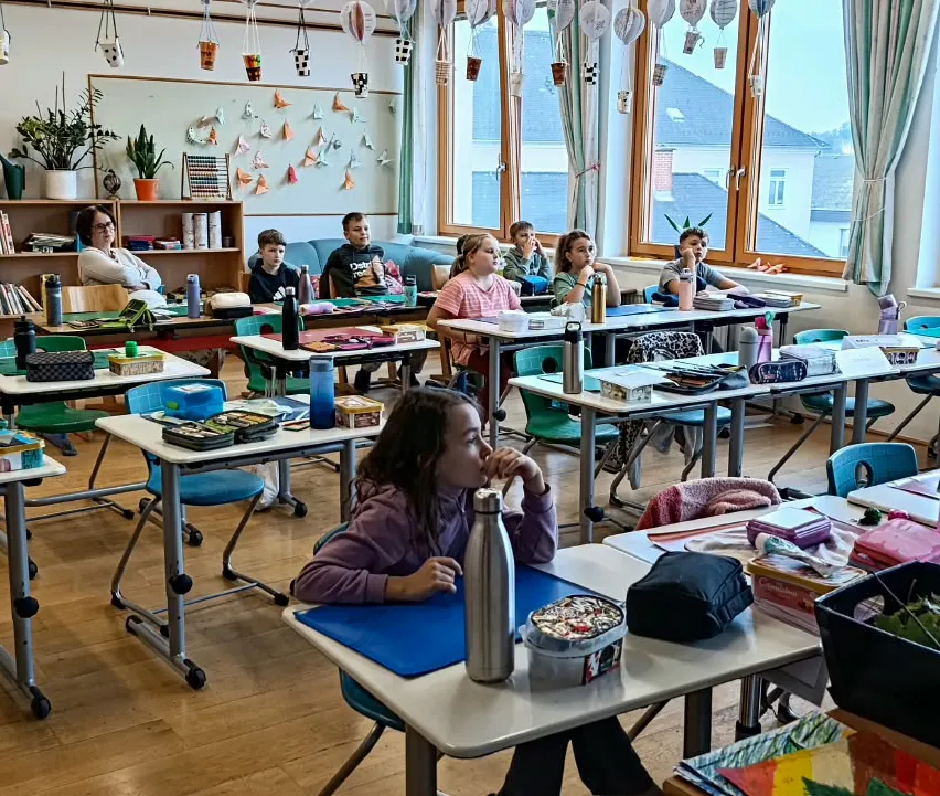 Ein Klassenzimmer mit Schülern, die an Tischen sitzen, ein Lehrer steht vor ihnen.