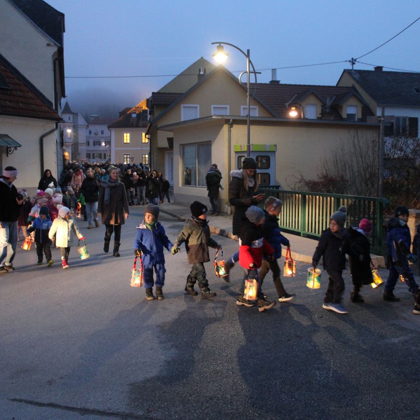 A group of children, illuminated by lanterns, walk down a street with houses and streetlights.