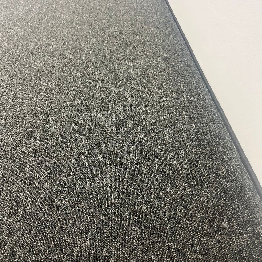 A close-up view of a gray carpet with a textured surface. The carpet has a smooth, shiny finish.