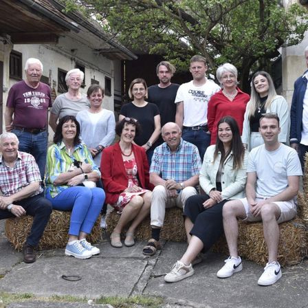 Eine Gruppe von Menschen, sowohl jung als auch alt, posiert für ein Foto vor einem Gebäude mit Heuballen auf dem Boden.