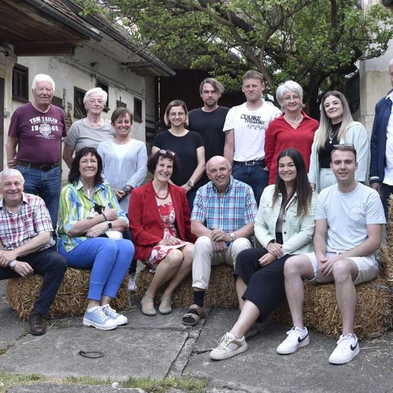 Eine Gruppe von Menschen, sowohl jung als auch alt, posiert für ein Foto vor einem Gebäude mit Heuballen auf dem Boden.