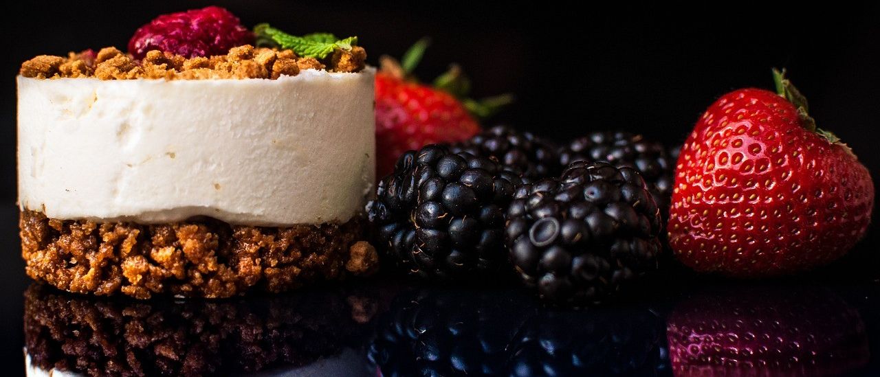 Nahaufnahme eines köstlichen Joghurtkuchens, gekrönt mit Beeren und Minzblättern vor dunklem Hintergrund.
