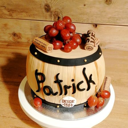 Ein fassförmiger Kuchen mit schwarzem Band, roten Trauben und Korken oben. Der Kuchen ist mit dem Namen Patrick und dem Jahr 1987 beschriftet.