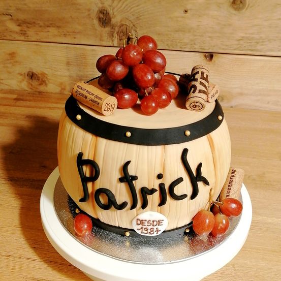 Ein fassförmiger Kuchen mit schwarzem Band, roten Trauben und Korken oben. Der Kuchen ist mit dem Namen Patrick und dem Jahr 1987 beschriftet.