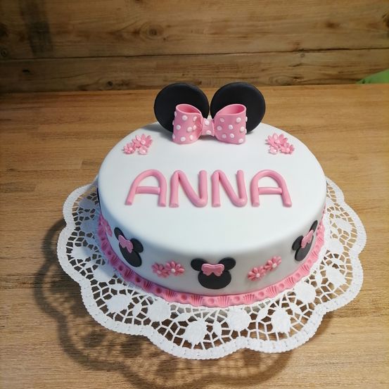 Ein rosa und weißer Minnie-Mouse-Geburtstagskuchen mit dem Namen Anna in rosa Zuckerguss auf einem Holztisch.