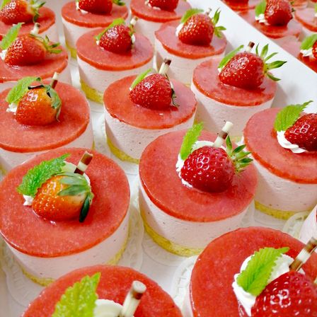 Eine Nahaufnahme mehrerer Erdbeertörtchen auf einem weißen Tablett, jedes mit einer Erdbeere und einem Minzblatt garniert.