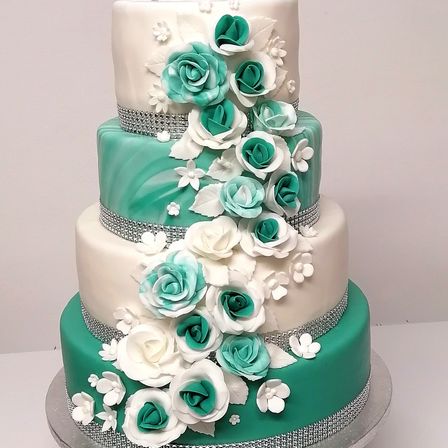 Ein dreistufiger Hochzeitskuchen mit weißen und türkisen Rosen, Silber- und weißen Dekorationen und einem Silber- und weißen Rand.