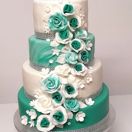 Ein dreistufiger Hochzeitskuchen mit weißen und türkisen Rosen, Silber- und weißen Dekorationen und einem Silber- und weißen Rand.
