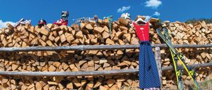Ein Holzzaun hält einen großen Stapel Brennholz, mit Skiern und verschiedener Wintersportausrüstung obenauf.