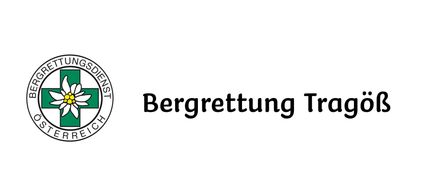 Das Bild zeigt ein Logo für Bergrettung Tragöß, eine österreichische Bergrettungsorganisation, mit einem stilisierten weißen Kreuz, einer gelben Blume in der Mitte und dem Wort 'Bergrettung Tragöß' in Fettschrift darunter.