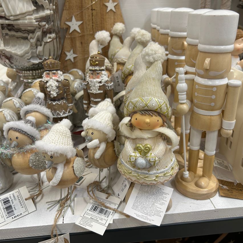 Eine Ausstellung von Weihnachtsdekorationen umfasst eine Vielzahl von Figuren, darunter Nussknacker, Weihnachtsmänner, Vögel und einen Gnom, alle mit weißen und goldenen Akzenten verziert.