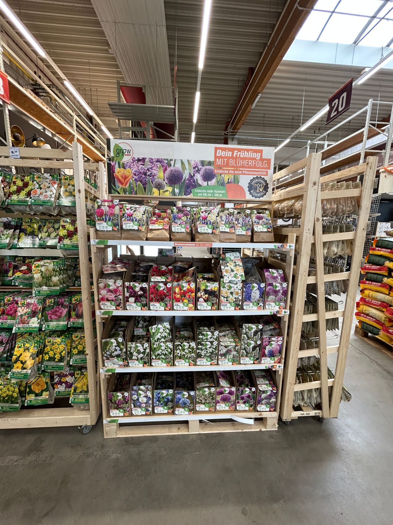 Ein Geschäft voller verschiedener Blumensamen in beschrifteten Verpackungen. Ein großes Schild auf Deutsch befindet sich oben auf dem Display.