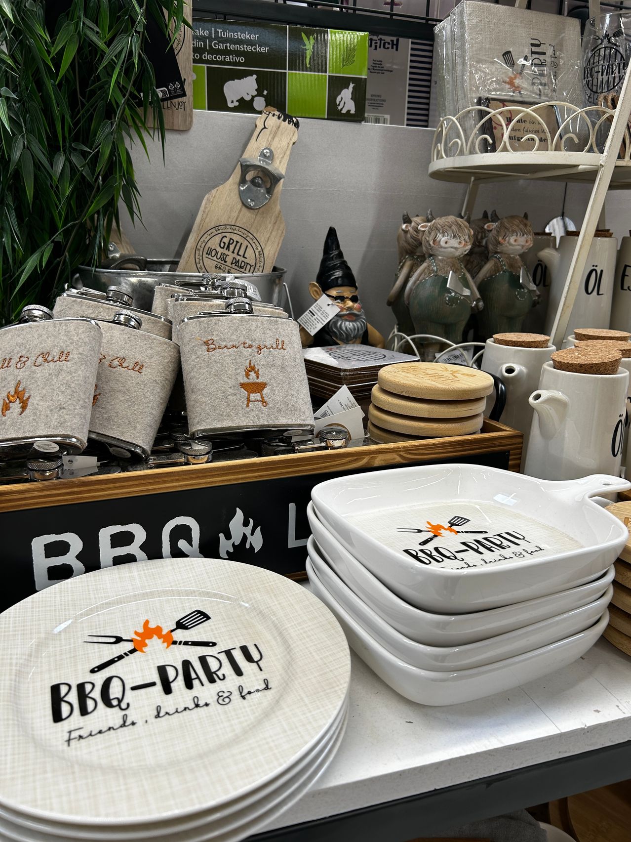 Eine Ausstellung von BBQ-thematischem Küchenzubehör, einschließlich Teller, Flakons und Tassen, auf einem Holzregal mit einem Schild, das BBQ besagt.