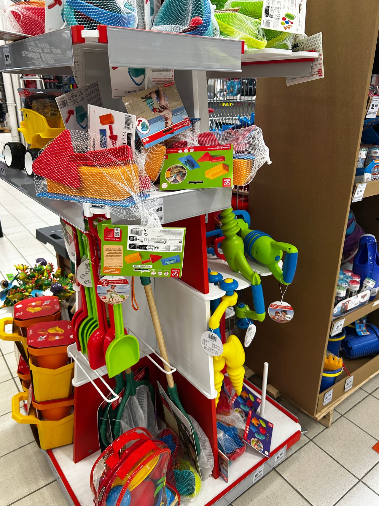 Eine Ausstellung von Strandspielzeug in einem Geschäft, einschließlich Eimer, Schaufeln und Netze, auf Regalen angeordnet und einige hängend.