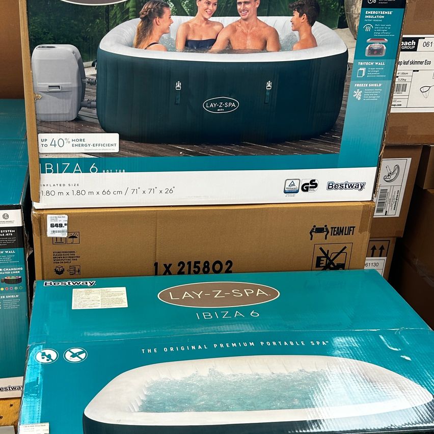 Eine blaue Box des Lay-Z-Spa Ibiza 6 Whirlpools mit einem Bild von drei Personen im Inneren des Whirlpools. Die Box liegt auf anderen Boxen.