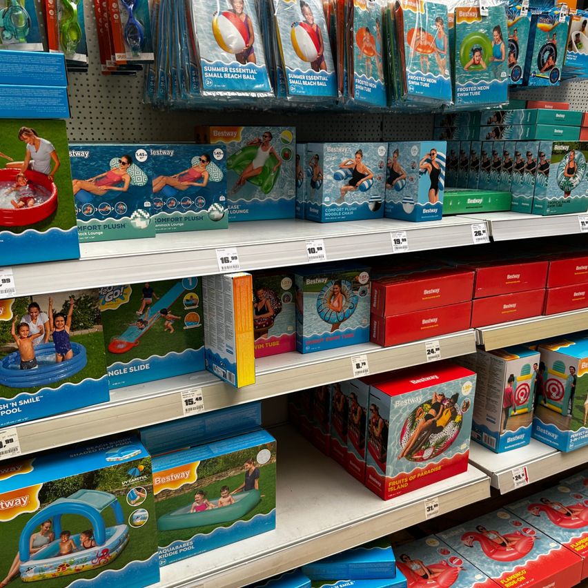 Ein Ladenregal zeigt verschiedene aufblasbare Poolprodukte, einschließlich Liegestühle, Rutschen und kleine Strandbälle, alles in blauer und roter Verpackung.