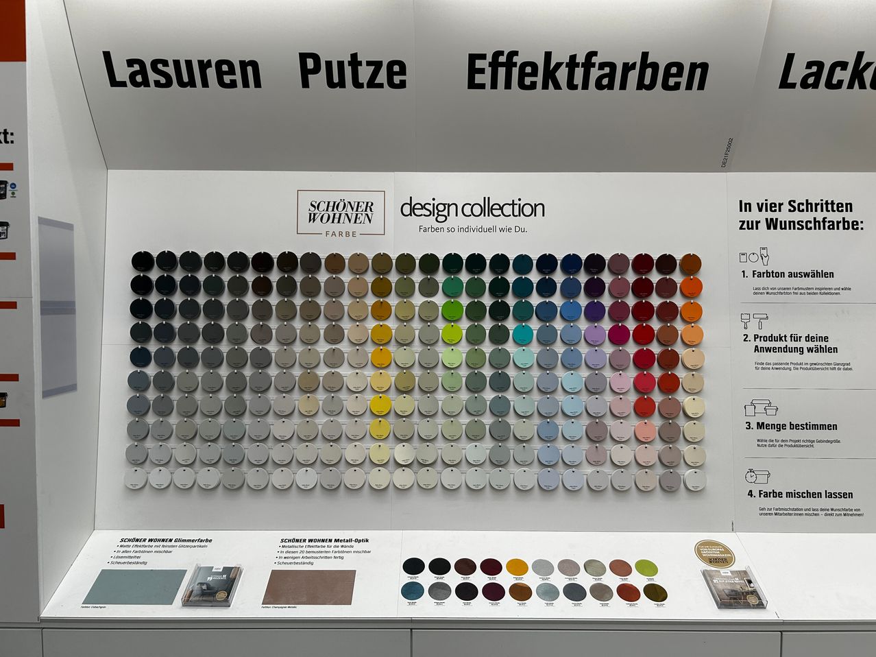 Eine Wand, die eine große Sammlung von gefärbten Farbmustern zeigt, unterteilt in Abschnitte für 'Lasuren Putze', 'Effektfarben' und 'Schöner Wohnen'. Die Muster sind in Reihen und Spalten angeordnet, mit Etiketten, die ihre Namen und Kategorien angeben.