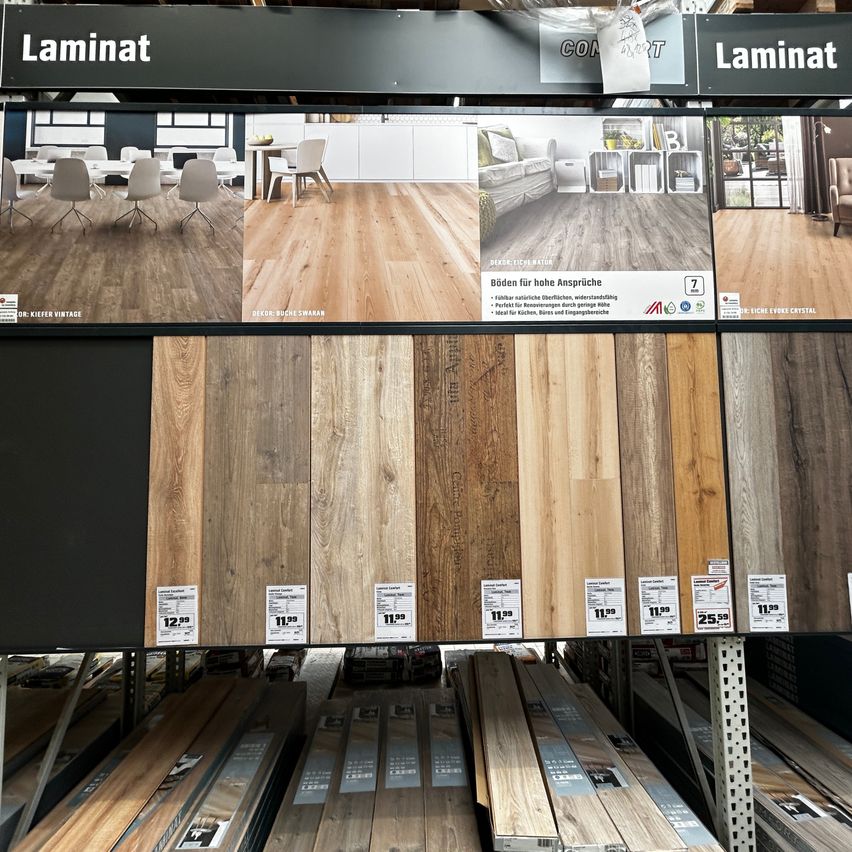 Ein Ladendisplay mit verschiedenen Laminatbodenoptionen, einschließlich verschiedener Holztexturen und Farben, mit Preisschildern und einem Schild, das 'Laminat' anzeigt.