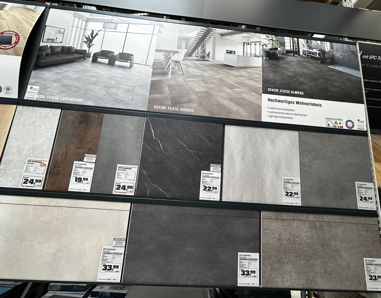 Eine Ausstellung verschiedener Fliesenoptionen mit Preisschildern und einem Hintergrundbild eines Wohnzimmers. Die Fliesen sind in verschiedenen Farben und Stilen.
