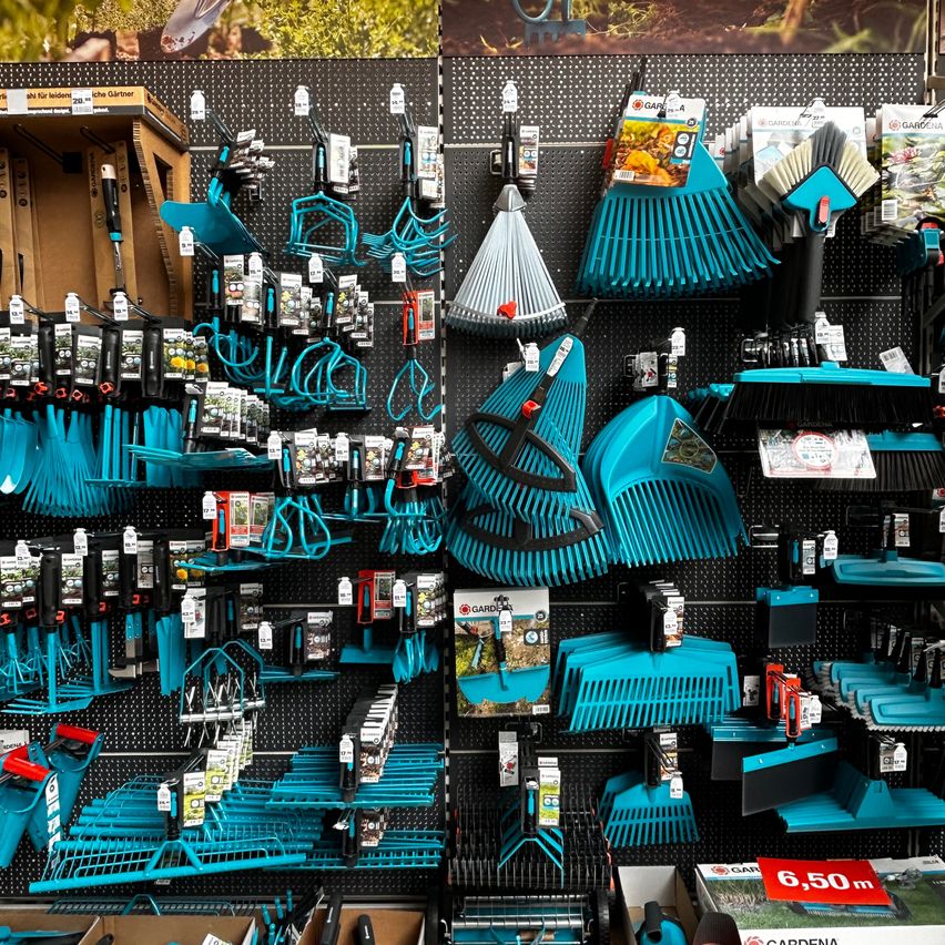 A store display featuring a variety of blue gardening tools, including rakes, shovels, and other equipment, neatly organized on a black pegboard.