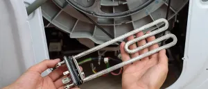 Eine Person entfernt ein Heizelement aus einer Waschmaschine. Das Element ist mit Kabeln verbunden. Die Tür der Waschmaschine ist geöffnet.