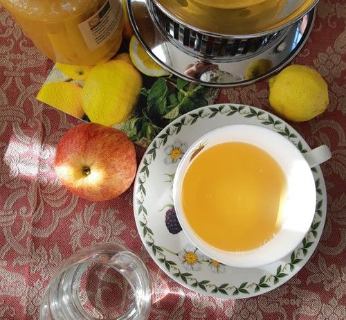 Eine Tasse Tee steht auf einer Untertasse mit Zitronen und Äpfeln auf dem Tisch, neben einem Glas Honig.