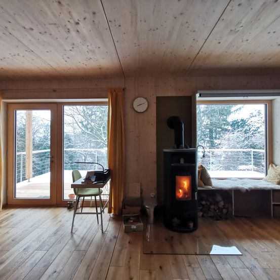 Ein Holzinnenraum mit Kamin, Schreibtisch und Fenster mit Blick auf den Balkon. Es gibt eine Uhr und eine Bank mit Kissen.