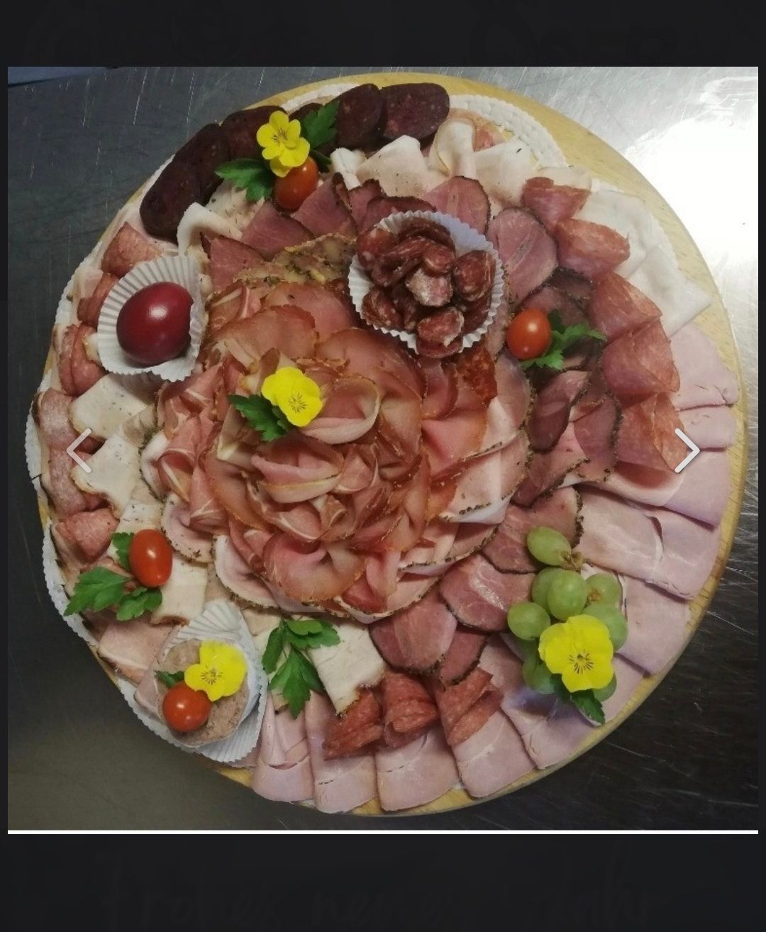 Eine runde Charcuterie-Platte mit verschiedenen Fleisch- und Käsesorten, verziert mit Blumen und Kräutern.