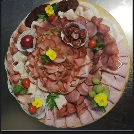 Eine runde Charcuterie-Platte mit verschiedenen Fleisch- und Käsesorten, verziert mit Blumen und Kräutern.