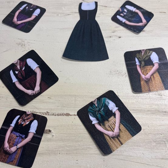 Ein Tisch mit acht quadratischen Matten, jede mit einem anderen Bild einer Frau in einem traditionellen Kleid mit einem Schal, in einem Kreis angeordnet.