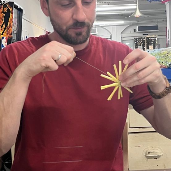 Ein Mann in einem roten Shirt arbeitet an einem gelben Objekt mit den Händen. Er befindet sich in einem Innenraum mit einem Basketballposter an der Wand.