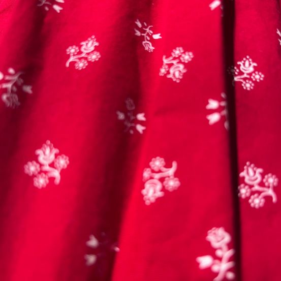 Eine Nahaufnahme eines roten Stoffes mit weißen Blumenmustern, leicht verschwommen, zeigt das komplizierte Design und die lebendige Farbe.