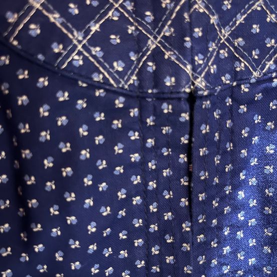 Ein Nahaufnahme von einem blauen Stoff mit kleinen weißen Blumenmustern und einem rautenförmigen Muster, das mit weißen Fäden genäht wurde.