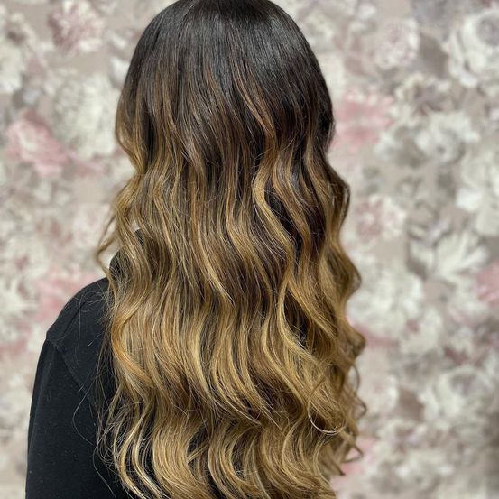 Eine Frau mit langen, gewellten blonden Haaren in einem lockeren, natürlichen Look, trägt ein schwarzes Oberteil.