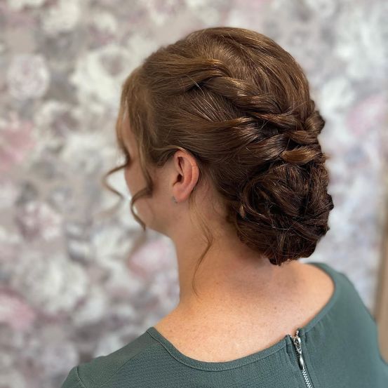 Eine Frau mit braunen Haaren in einem geflochtenen Hochsteckfrisur, vor einem floralen Hintergrund.