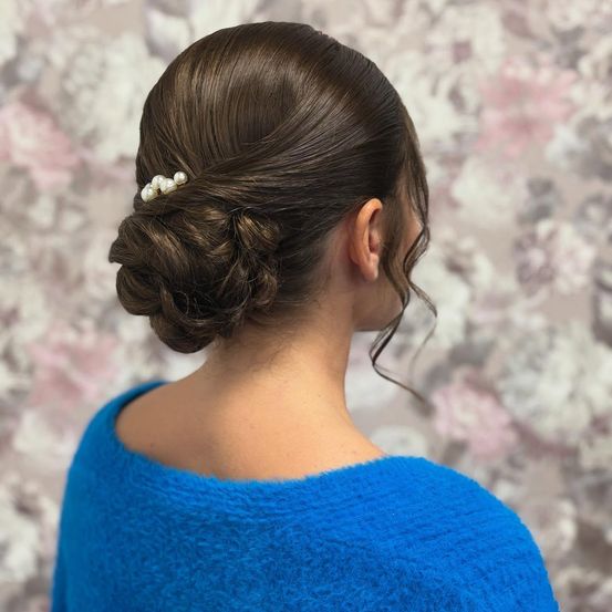 Eine Frau mit braunen Haaren, die in einem Dutt mit einer Perlenhaarnadel gestylt sind. Sie trägt einen blauen Pullover.