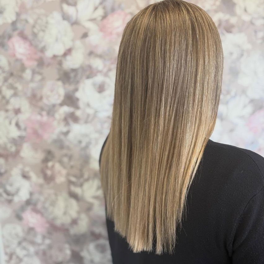 Eine Frau mit langen, glatten blonden Haaren in einem glatten, geraden Schnitt, vor einer floralen Tapete.