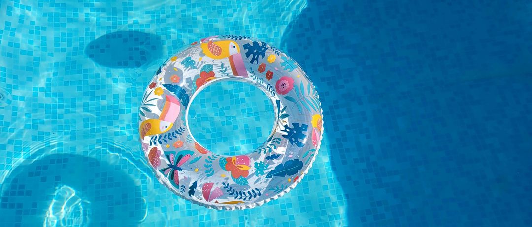 Ein bunter Schwimmreifen mit Blumen- und Tierdruck schwimmt in einem blau gefliesten Pool.