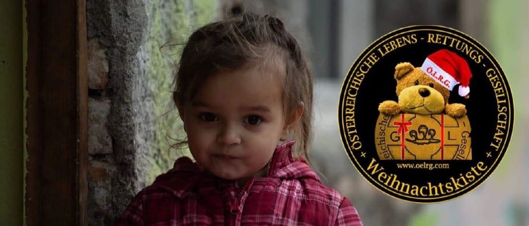 Ein Werbeplakat für O.L.R.G. Weihnachtskiste zeigt ein Kind mit einem Geschenkkarton. Es betont die Bedeutung der Erfüllung von Kinderträumen und ermutigt zu Spenden von Geschenkboxen. Der Text gibt Hinweise zum Verpacken von Geschenken und nennt einen Abgabeort.