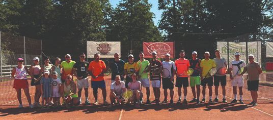 Eine Gruppe von Menschen in leuchtenden Farben posiert für ein Foto auf einem Tennisplatz mit Bannern im Hintergrund.