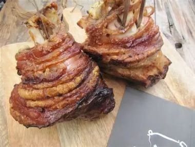 Zwei Scheiben schinkenverpacktes Fleisch, möglicherweise Schinken, auf einem Holzschneidebrett mit einer grauen Karte.