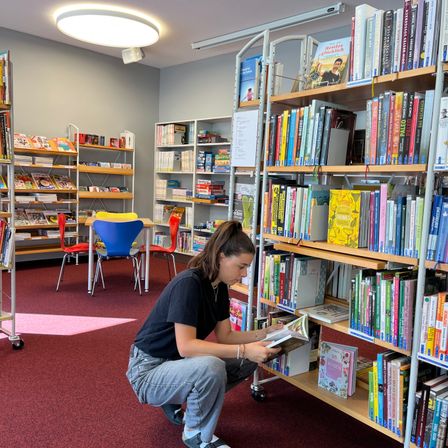 Bild enthält, Book, Library, Publication, Furniture, Person, Building, Bookcase, Chair, Shoe, Face