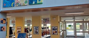 Das Innere eines Gebäudes mit gelben Wänden, das verschiedene farbenfrohe Kunstwerke und Bilder an den Wänden zeigt. Ein blaues Banner mit einem Design steht auf dem Boden. Eine Bank ist in der Nähe der Wand mit einem Schild platziert.