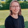 Eine Frau mit Brille und einem schwarzen T-Shirt steht draußen und lächelt.