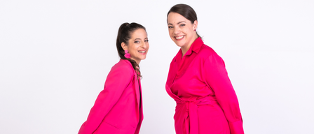 Zwei Frauen stehen und lächeln für ein Foto. Beide tragen rosa Anzüge. Die Frau auf der linken Seite hat ihr Haar hochgebunden und trägt rosa Ohrringe. Die Frau auf der rechten Seite trägt einen rosa Bademantel.