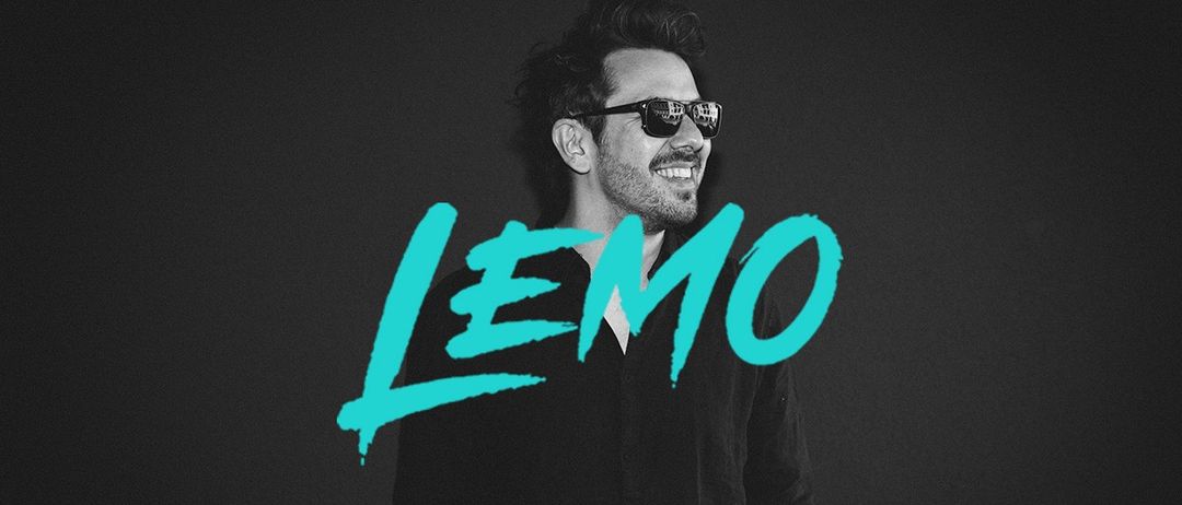 Ein lächelnder Mann in Sonnenbrille und schwarzem Shirt posiert für ein Bild mit dem Wort 'LEMO' in Türkis über ihm vor dunklem Hintergrund.