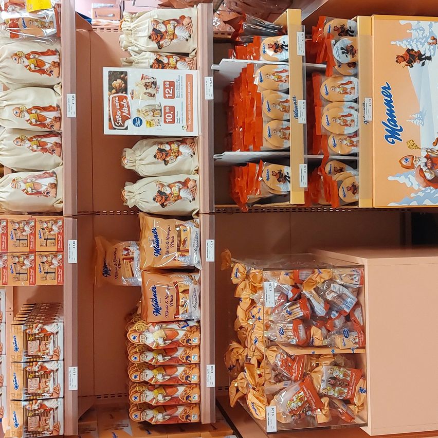 Ein Supermarktregal mit verschiedenen Produkten zur Schau gestellt. Die Regale enthalten Beutel mit Keksen und Snacks, einschließlich solcher der Marke Manner. Die Produkte sind in Plastikverpackungen mit Etiketten.