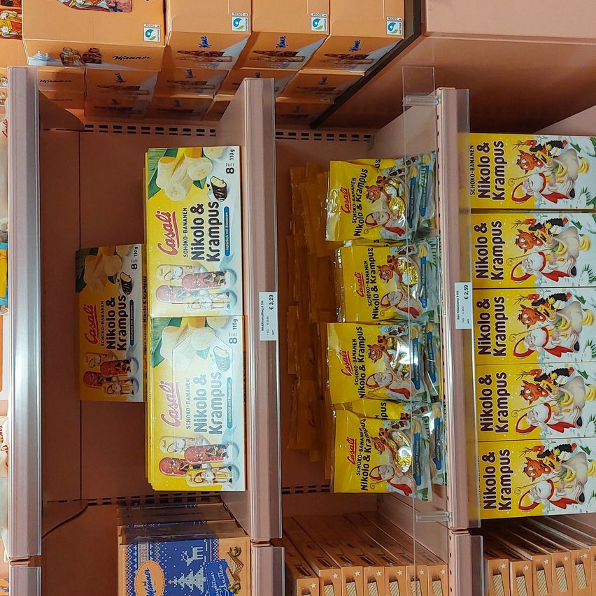 Ein Ladenregal zeigt Schachteln mit Nikolaus- und Krampus-Snacks, einschließlich bananengeschmackiger Snacks. Die Regale sind gefüllt mit verschiedenen Schachteln und Tüten mit Snacks, wobei Nikolaus- und Krampus-Figuren auf den Verpackungen abgebildet sind.