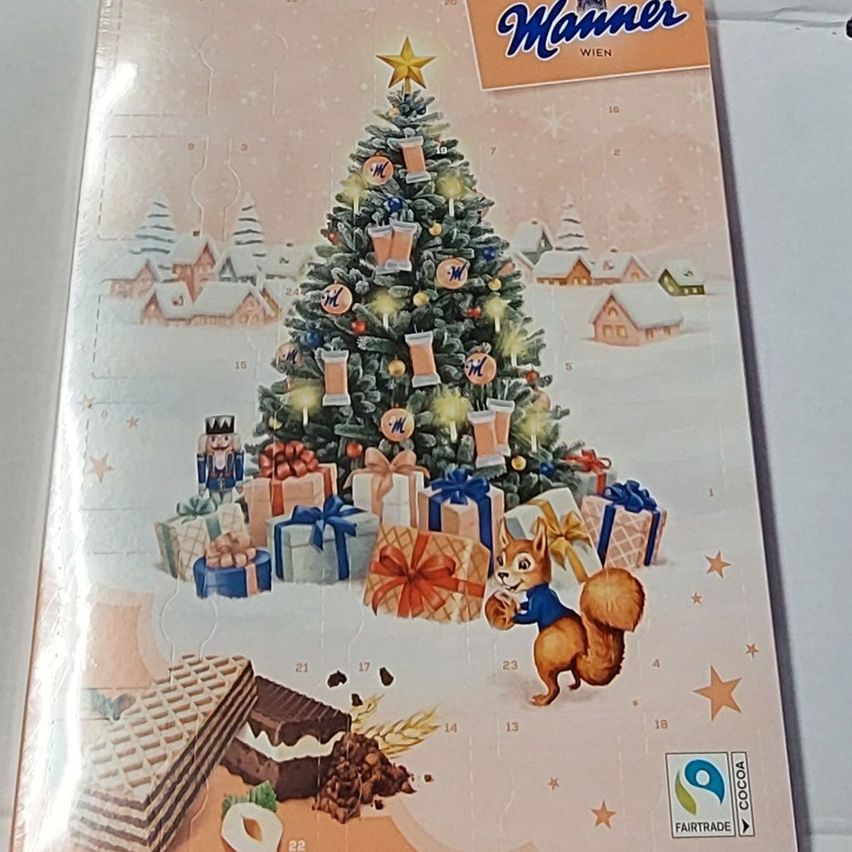 Ein festlicher Kalender zeigt einen geschmückten Weihnachtsbaum mit einem Eichhörnchen, Geschenken und einem Lebkuchenhaus. Es enthält Schokoladen, Waffeln und Sterne. Der Kalender wird von Manner gesponsert und trägt das Fairtrade-Zertifikat.